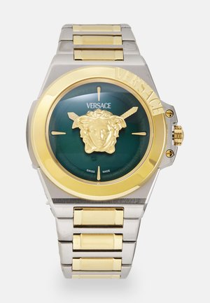 Montre Versace avec un cadran rond vert, emblème Méduse doré, bracelet en or et argent, boîtier en acier inoxydable et logo Versace bien en évidence.