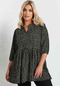Blusa nera con macchie bianche, vita arricciata e scollatura a V. Maniche a tre quarti e un design fluido creano una silhouette rilassata.