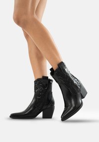 Botas negras de cuero hasta el tobillo con puntas afiladas, acentos texturizados en relieve, cremallera lateral y un tacón bloque moderado.