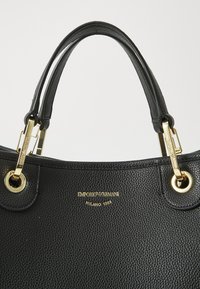 Sac à main Emporio Armani en cuir noir texturé avec doubles poignées et détails métalliques dorés.