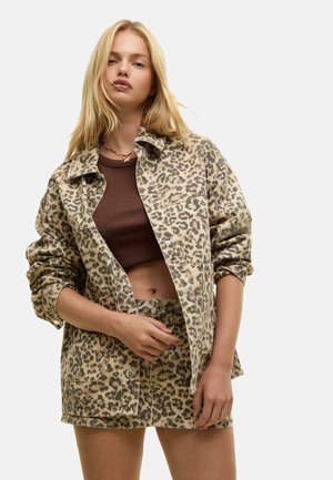Giacca a stampa leopardo in beige con bottoni e tasche frontali, abbinata a un top marrone e una mini gonna coordinata. Tessuto dalla superficie liscia.