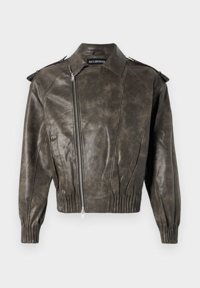 Ελιά πράσινη δερμάτινη τζάacket με κοντή εφαρμογή, φερμουάρ στο κλείσιμο και δομημένους ώμους. Διαθέτει μαζεμένα διακοσμητικά στο μανίκι και στο στρίφωμα.