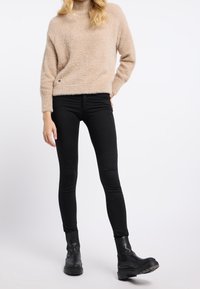 Beige fluffig tröja, hög krage, svarta skinny jeans och svarta ank stövlar med en kraftig sula. Enkelt design utan mönster eller detaljer.