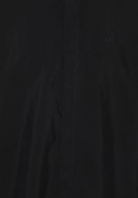 Maglietta nera realizzata in tessuto morbido, con un sottile logo A|X. Il design presenta una vestibilità classica con cuciture e dettagli minimi.