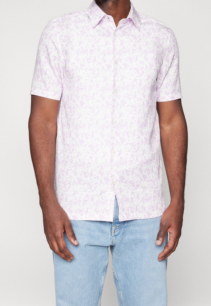 Koszula z krótkim rękawem w jasnofioletowym kolorze z kwiatowym wzorem, z kołnierzykiem zapinanym na guziki i prostym dołem, wykonana z lekkiego materiału.