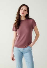 Kortærmet, tætsiddende top i mauve, lavet af tekstureret stof. Rund hals med diskrete sideslidser, parret med lyseblå jeans.