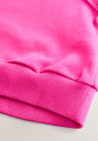 Hellpinkes Sweatshirt mit gerippten Bündchen und Saum, das eine glatte Textur und gleichmäßige Nähte zeigt. Nahaufnahme, mit Fokus auf die Detailansicht des Ärmels.