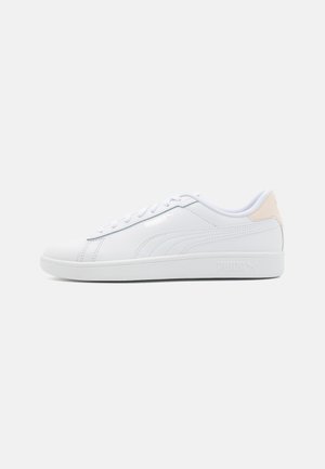 Zapatillas deportivas blancas de cuero sintético con textura suave, suela plana de goma y un sutil acento rosa en el talón.