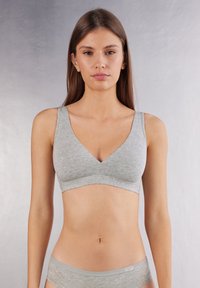 Bralette en coton gris avec un design en V, des bretelles larges et une finition sans couture. Il présente une texture douce et une esthétique minimaliste.