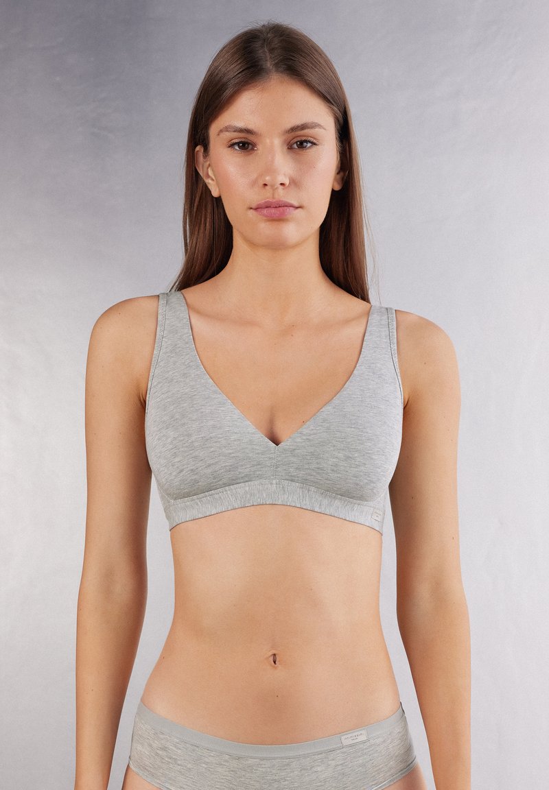 Bralette en coton gris avec un design en V, des bretelles larges et une finition sans couture. Il présente une texture douce et une esthétique minimaliste.