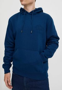 Navy blue pullover hoodie made of soft fabric, featuring a front kangaroo pocket and adjustable drawstrings with metal tips.