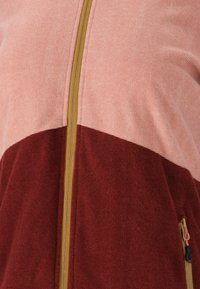 Veste zippée en color-block avec une section supérieure texturée rose et une section inférieure bordeaux, dotée d'une fermeture éclair dorée et de poches latérales.