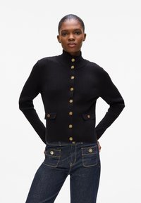 Cardigan nero a coste con colletto alto, dotato di bottoni in tonalità oro e due tasche frontali con dettagli hardware coordinati.