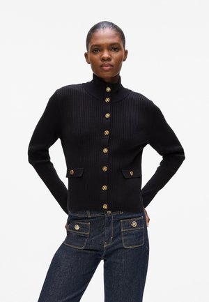 Black ribbed cardigan with a high collar, featuring gold-tone buttons and two front pockets with matching hardware details.
