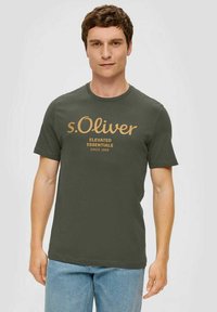 Olivgrünes Baumwoll-T-Shirt mit Rundhalsausschnitt, das auffälligen goldenen Drucktext zeigt: "s.Oliver" und "ELEVATED ESSENTIALS SINCE 1969."