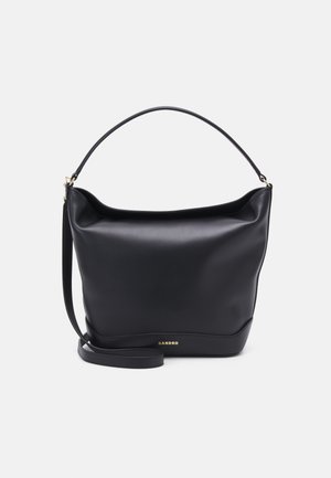 Sac bandoulière en cuir noir avec logo "SANDRO" doré, poignée supérieure incurvée et longue sangle réglable sur fond gris clair.