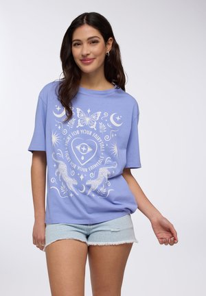 T-shirt in cotone blu chiaro con un design grafico bianco che presenta una farfalla, lune e leopardi, maniche corte e una vestibilità comoda.