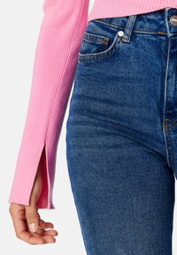 Top lungo a maniche ribbed rosa con spacco laterale abbinato a jeans in denim blu a vita alta con un classico design a cinque tasche.