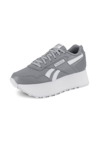 Sivé a biele sneakersy Reebok s hrubou bielou podrážkou a šnúrkami, z uhla, ktorý zobrazuje bočné pruhy a logo značky na boku a jazyku.