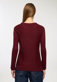 Burgundowy sweter z okrągłym dekoltem, długimi rękawami i ściągaczem. Dziany materiał oraz luźny krój, pokazany z tyłu.