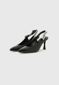 Black patent leather slingback heels with a pointed toe, slim heel, and contrasting black-and-white branded straps on the ankle.