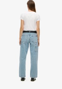 Jeans de mezclilla azul claro con un corte relajado, que cuentan con dos bolsillos traseros, un bolsillo lateral tipo cargo y un cinturón negro, combinados con una camiseta blanca.