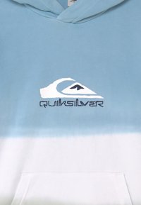 Hedvábně modrá a bílá gradientová mikina vyrobená z měkké tkaniny, s logem Quiksilver v bílé a černé barvě a s přední kapsou.