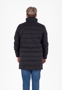 Cappotto imbottito nero con colletto alto, caratterizzato da cuciture orizzontali e maniche lunghe, abbinato a jeans in denim blu. Vista posteriore mostrata.