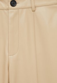 Pantalon beige en simili cuir avec une coupe droite, une seule poche avant et un détail bouton noir à la taille. Texture lisse.