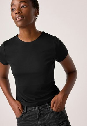 Black short-sleeve t-shirt with a round neckline, made from smooth fabric. Paired with dark patterned jeans, featuring a classic five-pocket design.