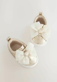 Metallisch goldene Sneakers mit einem floral geprägten Muster, einem großen weißen Schleifen vorne und einer weißen Gummisohle.