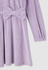 Fiołkowa sukienka z kordurowego materiału z dużą kokardą w talii, długimi rękawami i pionowym teksturowaniem. Doły wykończone są prostym ściegiem.