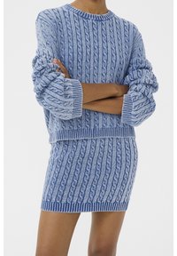 Ensemble composé d'un pull et d'une mini-jupe tricotés bleus, avec un motif en maille torsadée, des poignets et un ourlet côtelés épais, et des nuances de bleu variées sur l'ensemble.