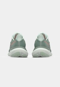 Zapatillas de running verdes con material superior texturizado, cuello acolchado y suela de goma. Presentan sutiles acentos en rosa y un diseño aerodinámico.