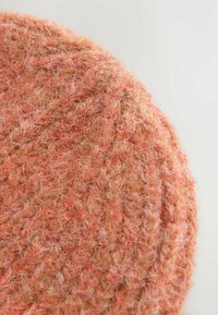 Ümmargune tekstiiltoode, millel on tekstuuriga pind heledates oranžides ja beežides toonides, iseloomustatud udusa, kootud mustriga.