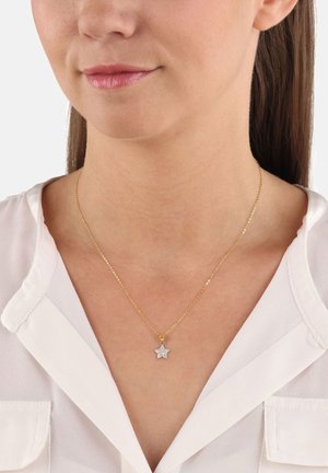 Gros plan sur une femme portant un collier en chaîne dorée avec un petit pendentif en forme d'étoile incrusté de pierres claires.