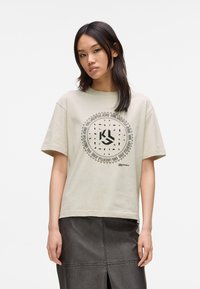 Jasnoszary bawełniany t-shirt z okrągłym czarnym wzorem graficznym umieszczonym na środku z przodu, połączony z ciemną skórzaną spódnicą z rozcięciem z tyłu.