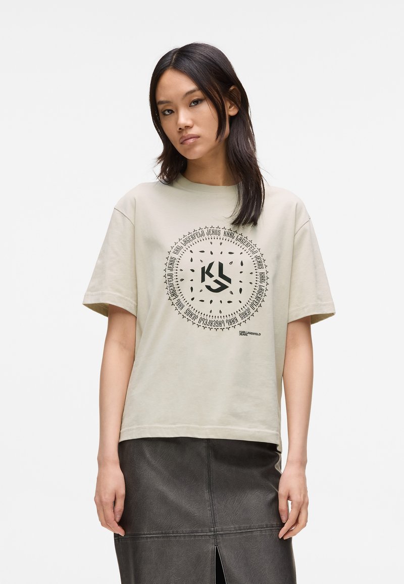 Jasnoszary bawełniany t-shirt z okrągłym czarnym wzorem graficznym umieszczonym na środku z przodu, połączony z ciemną skórzaną spódnicą z rozcięciem z tyłu.