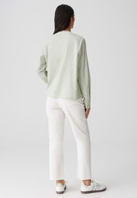 Camicia a maniche lunghe verde chiaro con una vestibilità rilassata, polsini abbottonati, abbinata a jeans bianchi a vita corta e sneakers bianche con accenti grigi.