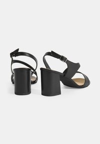 Zwarte hakken sandalen met een gesloten teen, open achterkant en kruissluiting ontwerp. Gemaakt van soepel leer met een stevige blokhak.