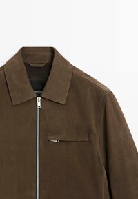 Braune Wildlederjacke mit spitzem Kragen und Reißverschluss vorne. Verfügt über eine Brusttasche und eine glatte Textur; modernes, minimalistisches Design.