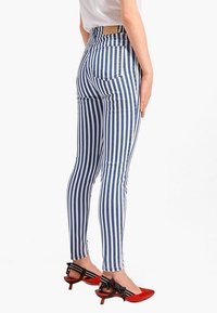 Höga, smala jeans i blå och vita vertikala ränder. Har två bakfickor och en åtsittande design. Matchas med röda spetsiga klackar.