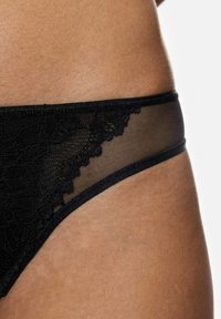 Culotte de bikini en dentelle noire avec un panneau en mesh transparent, des bords festonnés et une taille lisse, mettant en valeur une texture et un design complexes.