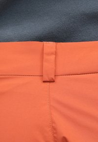 Oranje shorts met een soepele textuur, voorzien van een naadloze tailleband en een kleine lus. De achtergrond is een donkergrijze stof.