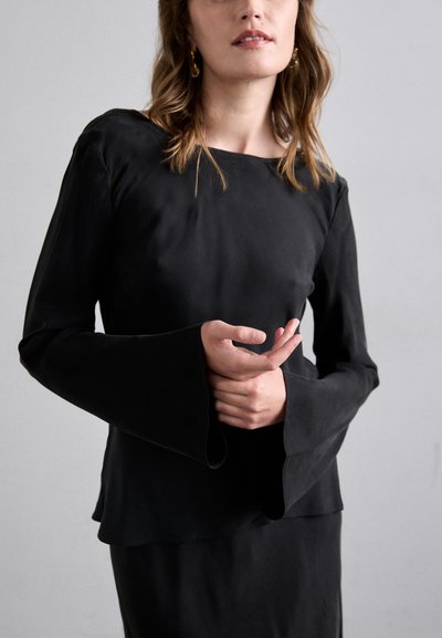 Haut noir à manches longues avec une texture lisse, doté d'un design de manches évasées larges et d'un ourlet superposé, associé à une jupe noire assortie.