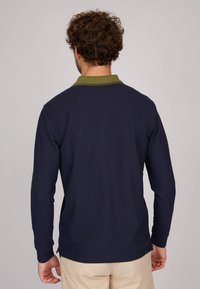 Polo à manches longues bleu marine avec un col vert. Texture côtelée, ourlet droit et détails de couture visibles. Ajustement flexible avec fentes latérales.