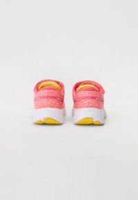 Rosa sportieve schoenen met een bovenwerk van gestructureerde stof, contrasterende gele binnenkant en een witte rubberen zool met gele gripdetails.