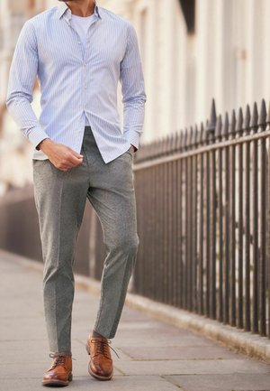 Chemise boutonnée bleu clair et blanche à rayures portée avec un pantalon gris texturé et des chaussures de ville en cuir marron, portées de manière décontractée dans la rue.