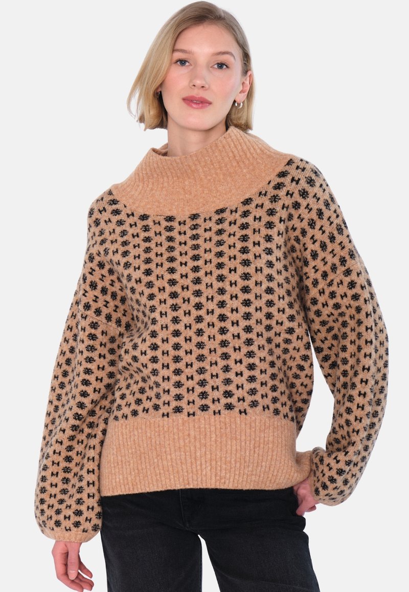 Beige stickad tröja med en bred, ribbad krage. Har svarta geometriska mönster över hela och ribbade muddar och fåll. Mjukt material.