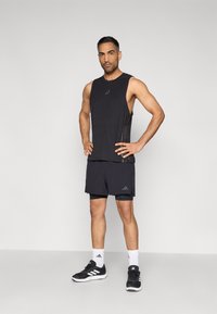 Μαύρο αθλητικό τοπ χωρίς μανίκια με διακριτική επωνυμία, σετ με ταιριαστά σορτς. Μαύρα αθλητικά παπούτσια και λευκές κάλτσες έως τον αστράγαλο ολοκληρώνουν την εμφάνιση.